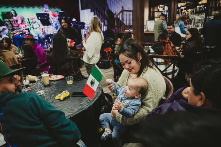 Noi Siriphone, an immigrant from Laos, and her partner, Ivan Morales, an immigrant from Mexico, laugh as their 9-month-old son, Zayne Morales, plays with a Mexican flag during a traditional holiday celebration in early December. (Meridith Kohut for The Wa